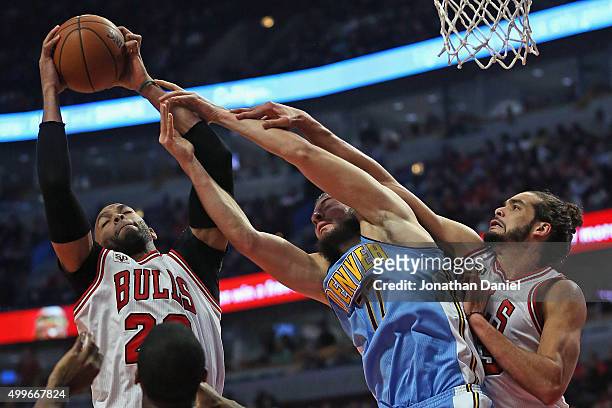 Taj Gibson of the Chicago Bulls grabs a rebound away from Joffrey Lauvergne of the Denver Nuggets as Joakim Noah applies defensive pressure at the...