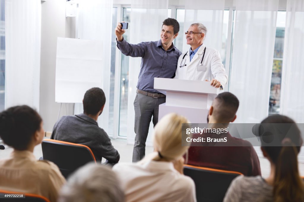Happy doctor and businessman taking a selfie on education event.