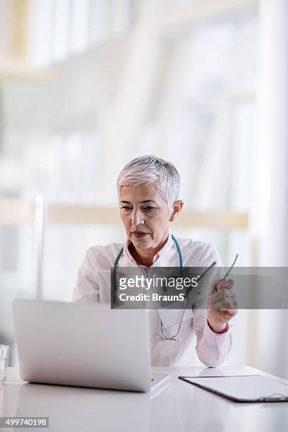 mature female doctor working on laptop in the office. - huisarts stockfoto's en -beelden