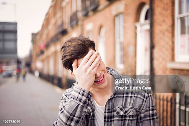 man covering his eyes in a laugh on the street - careless ストックフォトと画像