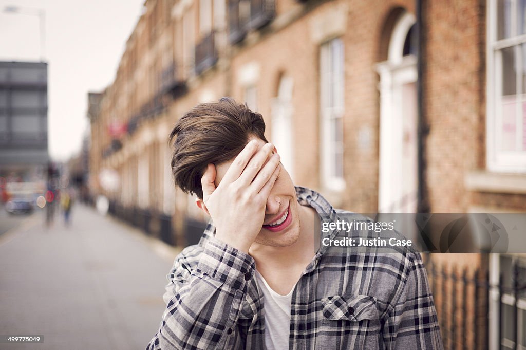 Man covering his eyes in a laugh on the street