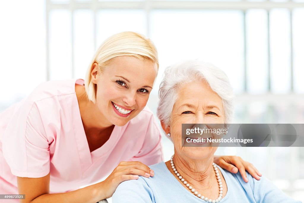 Nurse With Hands On Senior Patient's Shoulders In Nursing Home