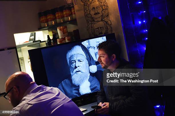 Jeremy Zunk, right, sits next to a television screen with the Christmas movie, "Miracle on 34th Street" at the holiday themed bar, Miracle on Seventh...