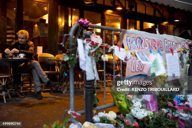 Man drinks a coffee on the terrace of the bar "A la Bonne Biere" during its reopening in Paris on December 4 behind a barrier with flowers, notes and...