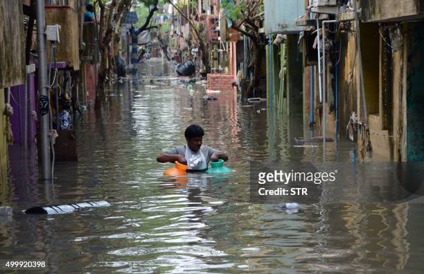 An Indian man carries gas canisters through floodwaters on a street in Chennai on December 4, 2015. Thousands of rescuers are racing to evacuate...