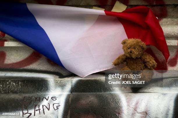 Picture taken on December 2, 2015 in Paris shows a cuddly toy and a French flag at a makeshift memorial in front of the statue of the Republique in...