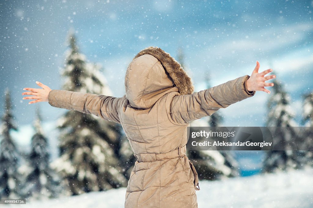 Giovane donna godendo inverno con le braccia sollevata mentre nevichi