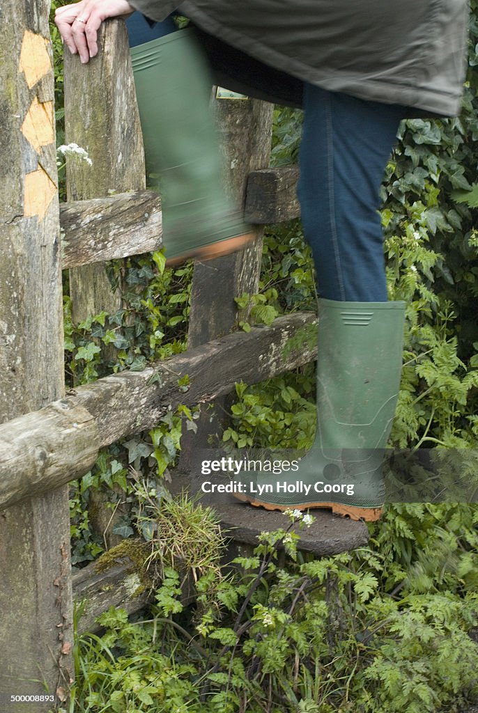 Woman in rubber boots climbing over wooden stile