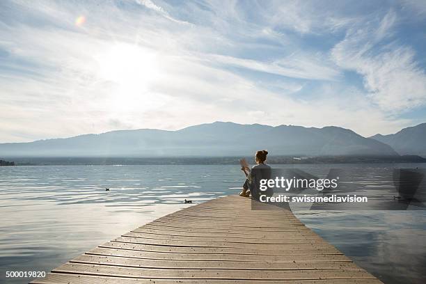 frau entspannt auf dem lake pier, liest ein buch - bootssteg stock-fotos und bilder