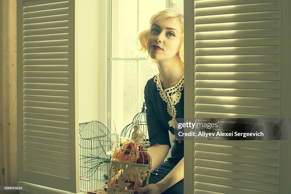 Caucasian woman holding birdcage in window