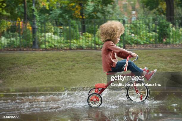 mixed race boy riding tricycle in park - tricycle stock-fotos und bilder