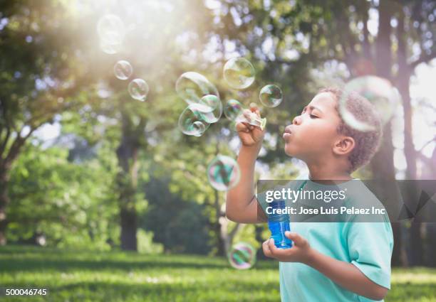 mixed race boy blowing bubbles outdoors - bubble wand foto e immagini stock