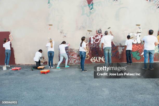 volunteers painting over graffiti wall - asistencia de la comunidad fotografías e imágenes de stock
