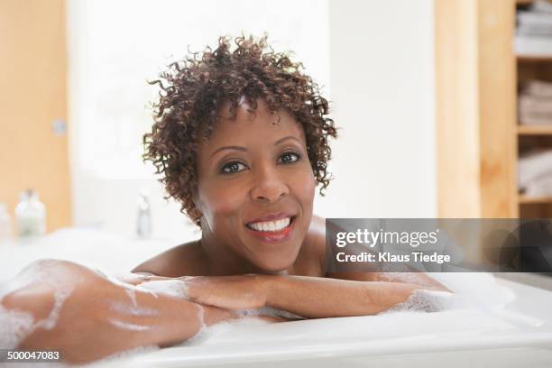 african american woman relaxing in bubble bath - woman bath bubbles stock-fotos und bilder
