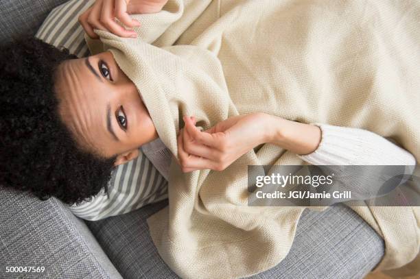 black woman wrapped in blanket on sofa - blanket photos et images de collection