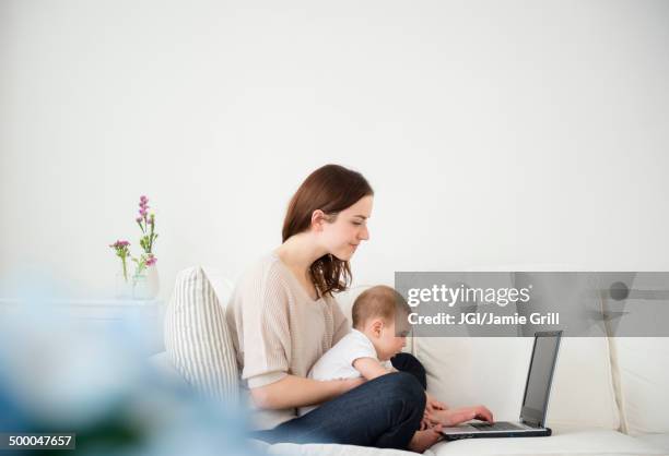 mother and baby using laptop on sofa - differential focus work stock pictures, royalty-free photos & images