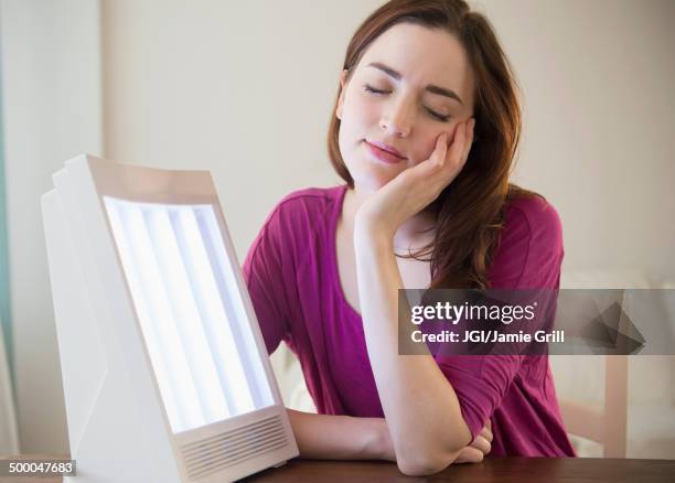 woman sitting by light therapy box - luminothérapie photos et images de collection