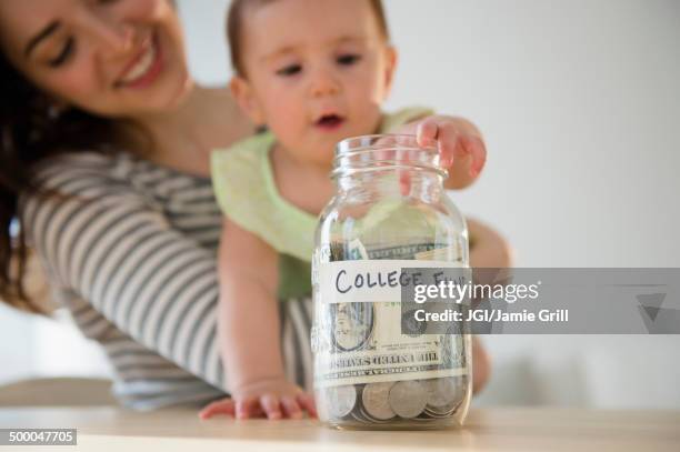 mother and baby putting money in college fund - save our future babies stock pictures, royalty-free photos & images