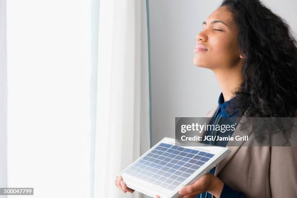 mixed race woman holding solar panel by window - seasonal affective disorder stock pictures, royalty-free photos & images