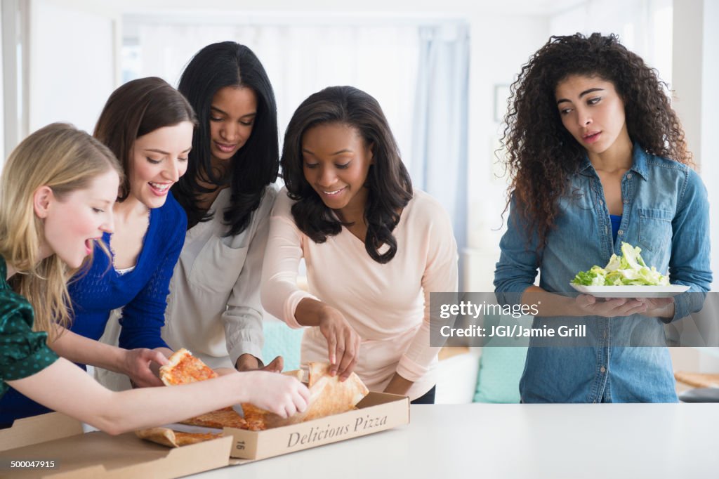 Woman with salad watching friends eat pizza