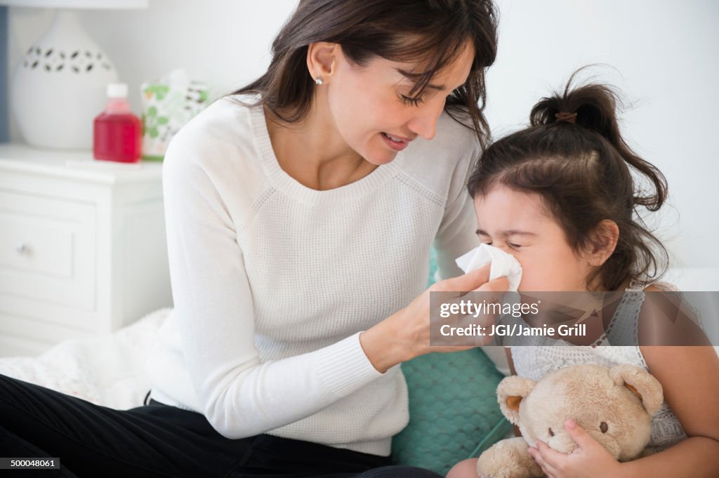 Hispanic mother wiping daughter's nose