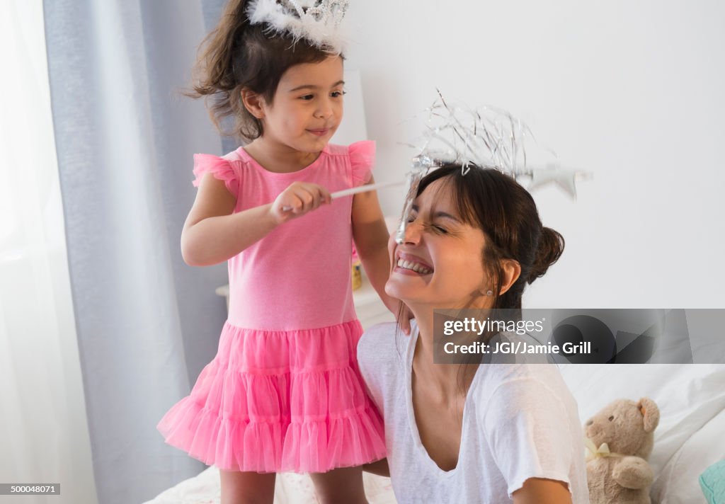Hispanic mother and daughter playing dress up on bed