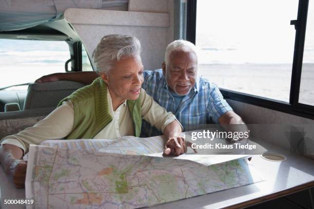 mixed race senior couple reading map in rv - rv beach foto e immagini stock