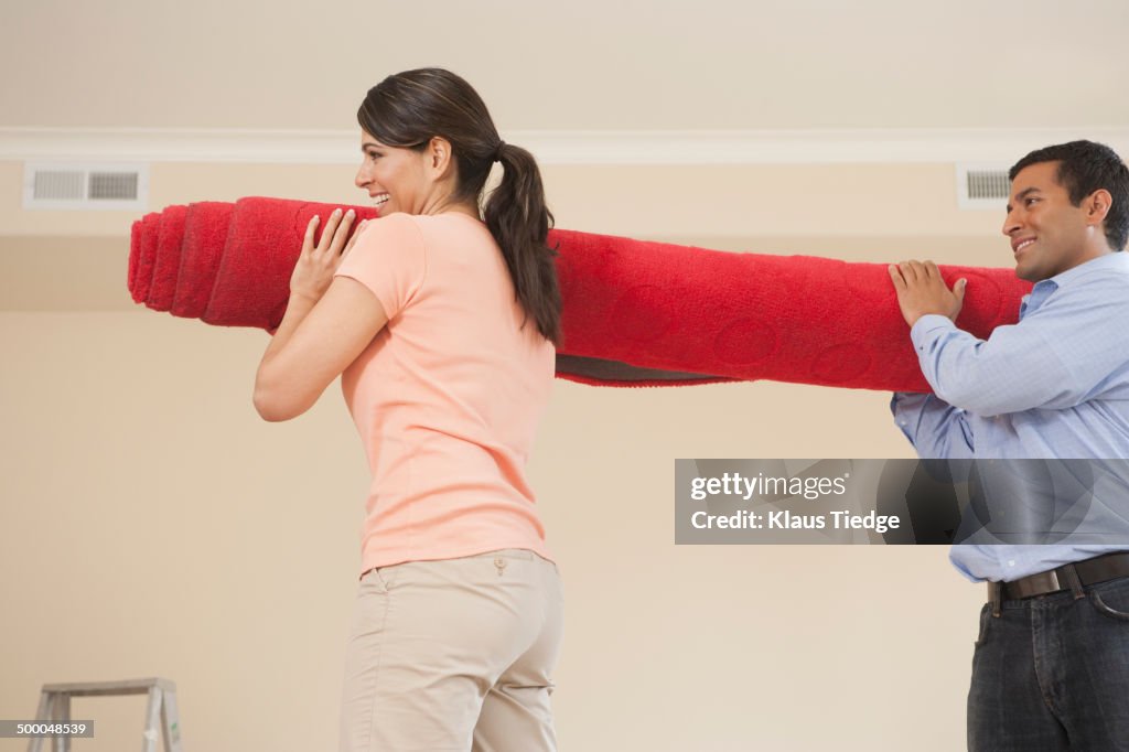 Hispanic couple carrying carpet in new home