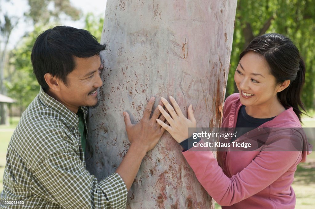 Asian couple hugging tree in park
