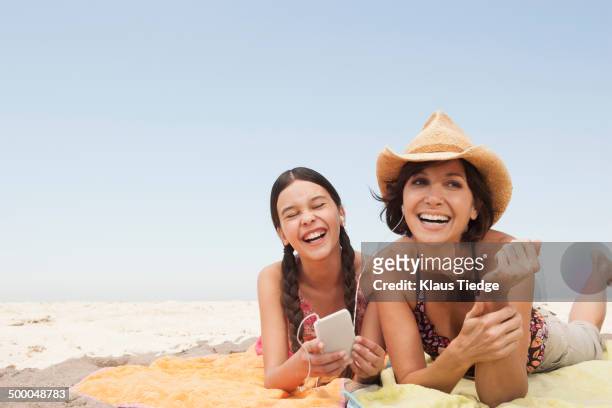 mother and daughter listening to headphones on beach - mother daughter towel fotografías e imágenes de stock