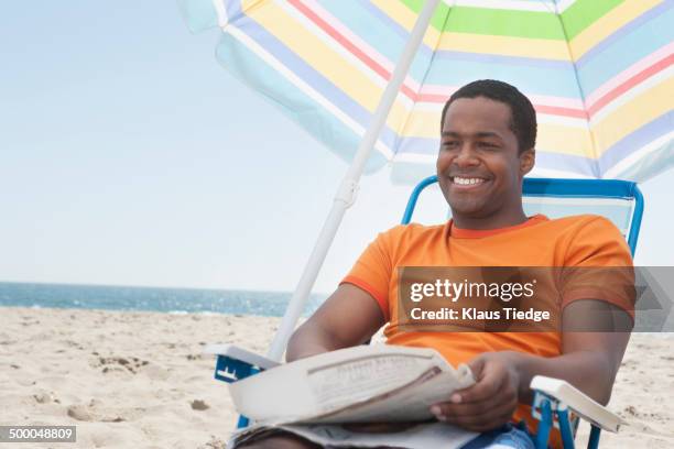 mixed race man sitting in lawn chair on beach - black man beach chair photos et images de collection