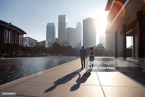 couple casting shadows on urban waterfront - downtown los angeles stock-fotos und bilder