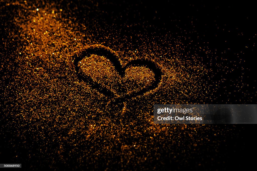 Heart shaped doodle drawn in golden colored glitter