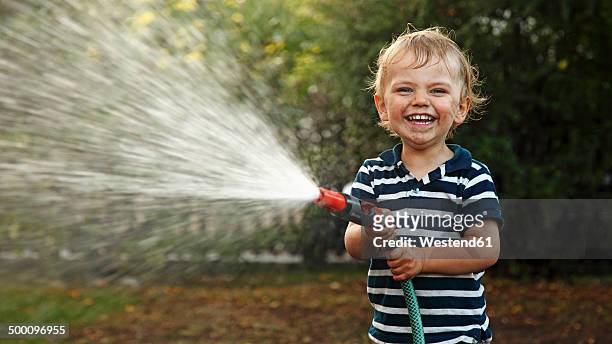 portrait of little boy splashing with garden hose - garden hose foto e immagini stock