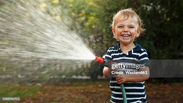 portrait of little boy splashing with garden hose - tuinslang stockfoto's en -beelden