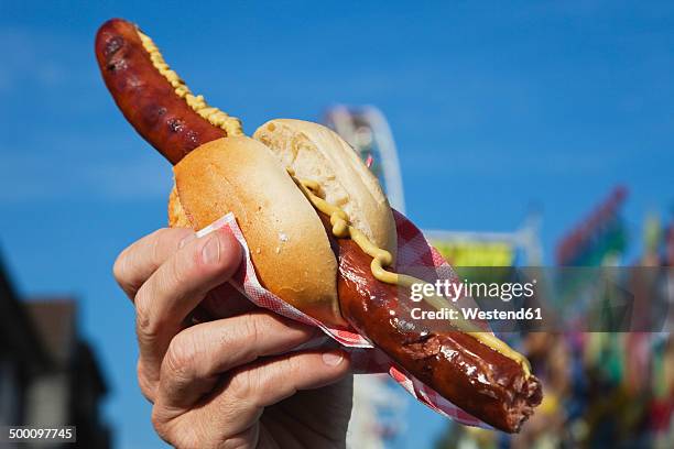 man holding sausage with roll in hand - german food stock-fotos und bilder