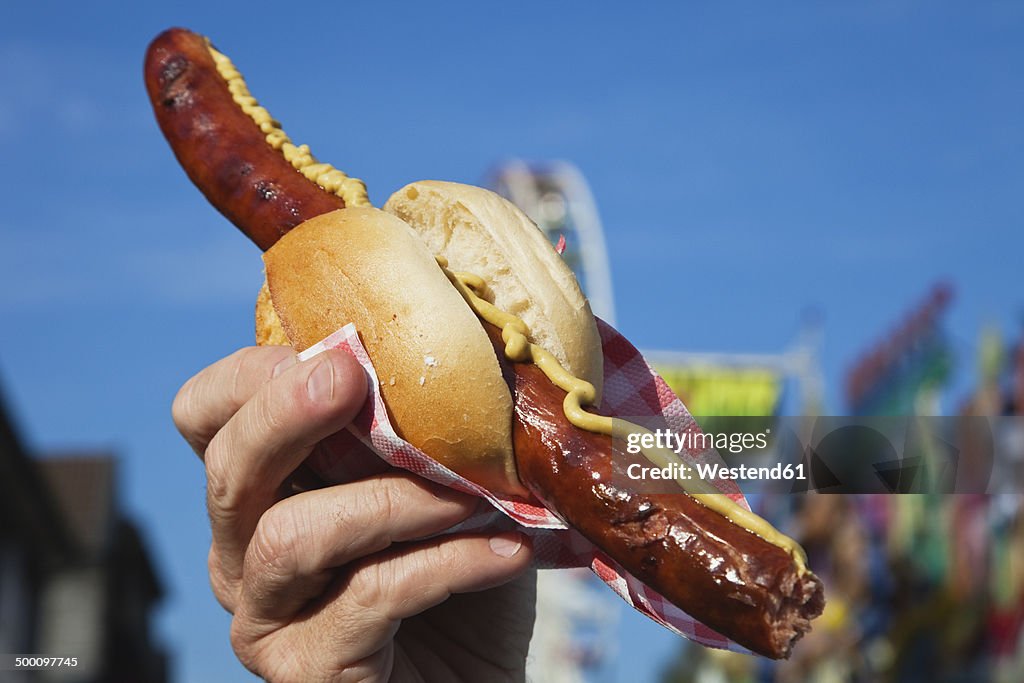 Man holding sausage with roll in hand