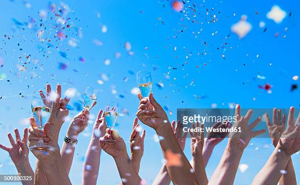 people exulting, arms raised with champagne glasses, confetti - young man arms up stock-fotos und bilder
