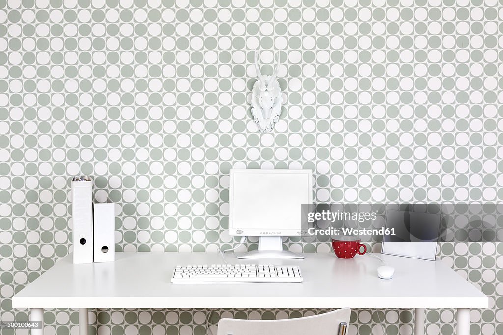 Desk at home office with white accessories in front of patterned wallpaper