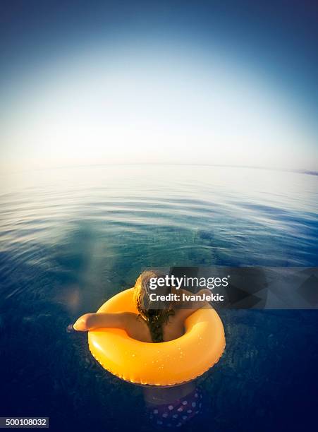 child floating on swimming tube in sea at twilight - zwemband stockfoto's en -beelden