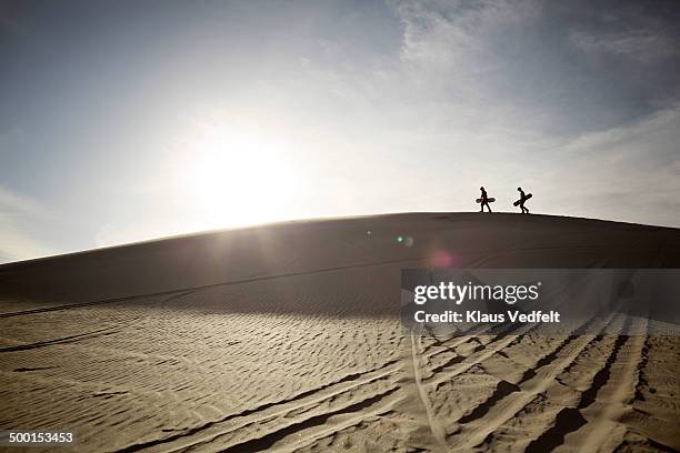 two sandboarders walking on the edge of sand dune - sand boarding stock pictures, royalty-free photos & images
