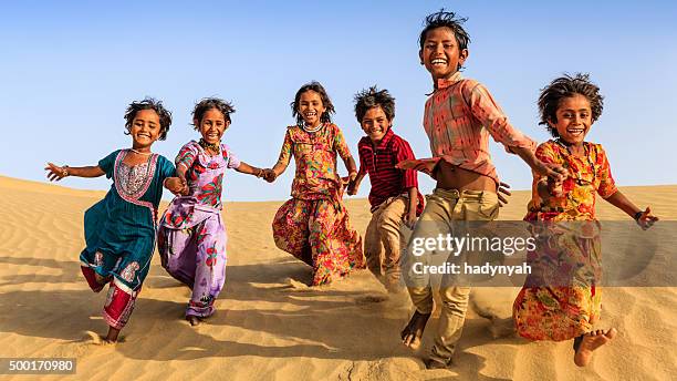 gruppe von glücklich indischen kinder laufen auf sand dune, indien - rajasthani youth stock-fotos und bilder