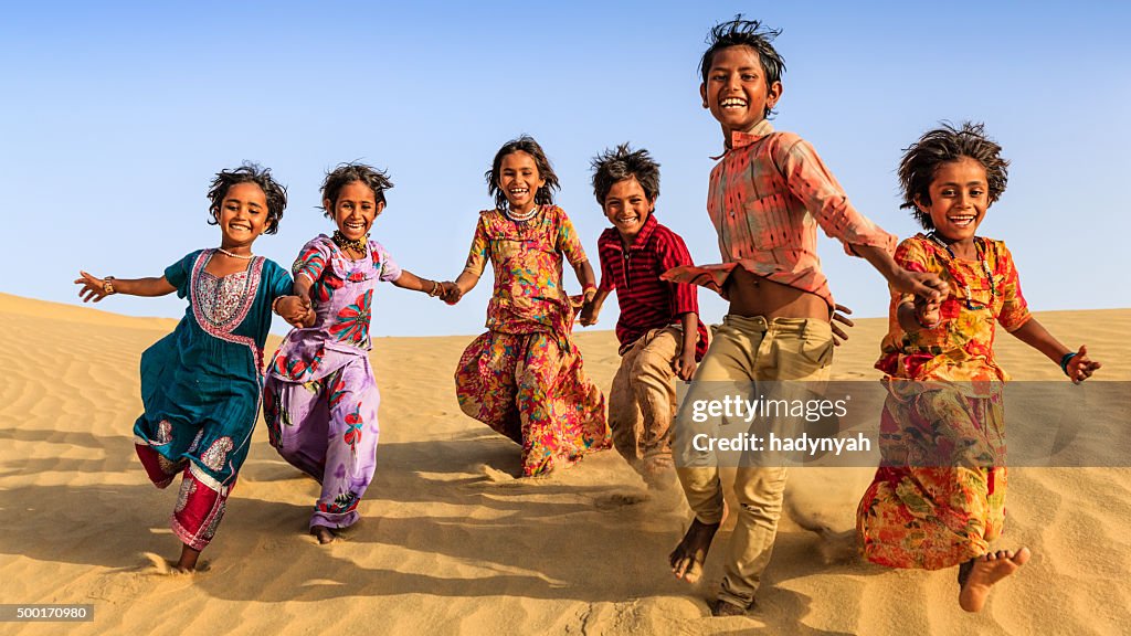 Group of happy Indian children running across sand dune, India