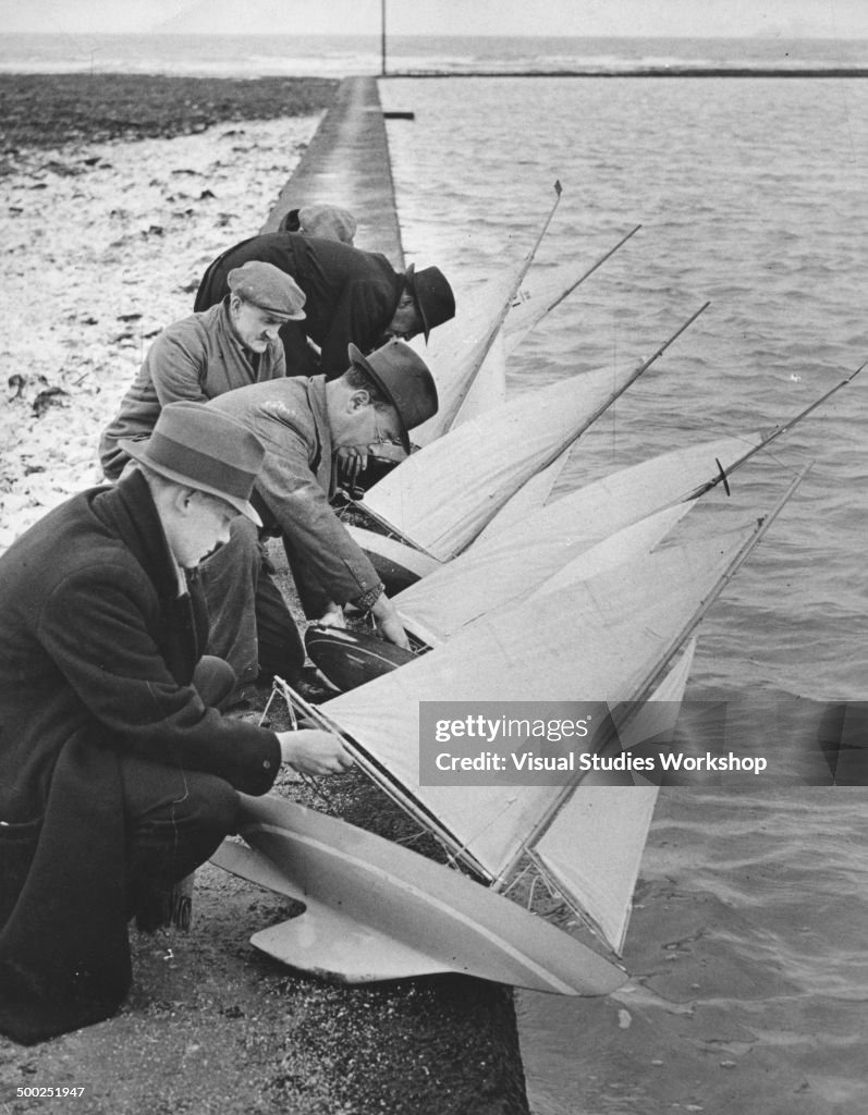 Men Make Adjustments To Model Sailboats