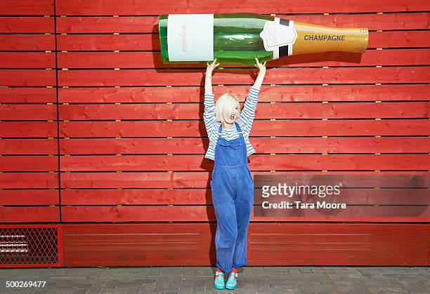 woman holding up giant champagne bottle - woman holding champagne stock-fotos und bilder