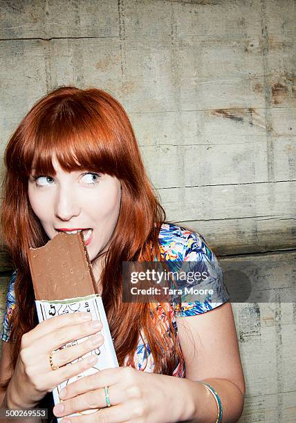 woman looking guilty eating chocolate bar - regret stock-fotos und bilder