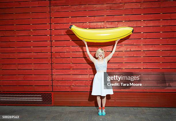 woman holding up giant toy banana - banane stock-fotos und bilder