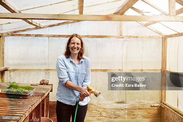 woman laughing and watering plants in a greenhouse - mid volwassen vrouw stockfoto's en -beelden