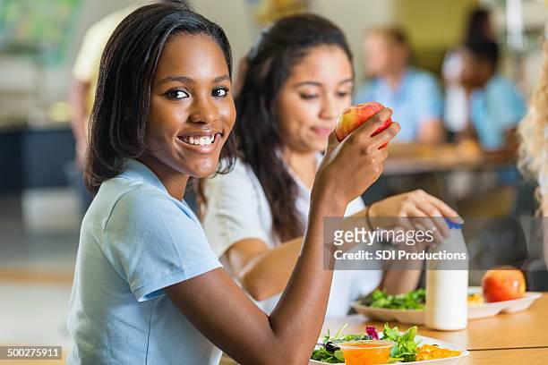 teenager eating healthy lunch with friends in school lunchroom - african american school uniform stock pictures, royalty-free photos & images