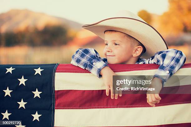 junge amerikanische cowboy mit us-flagge - boys in countryside stock-fotos und bilder